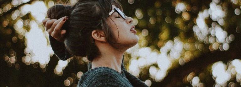 A woman standing surrounded by nature with her eyes closed