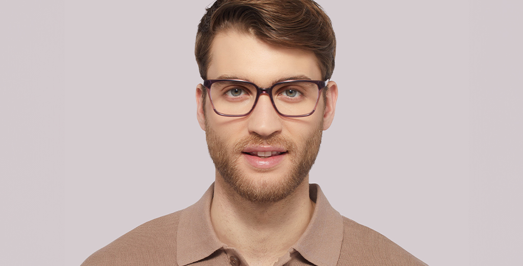 A man with wavy golden-brown hair and a short beard wearing purple acetate frames